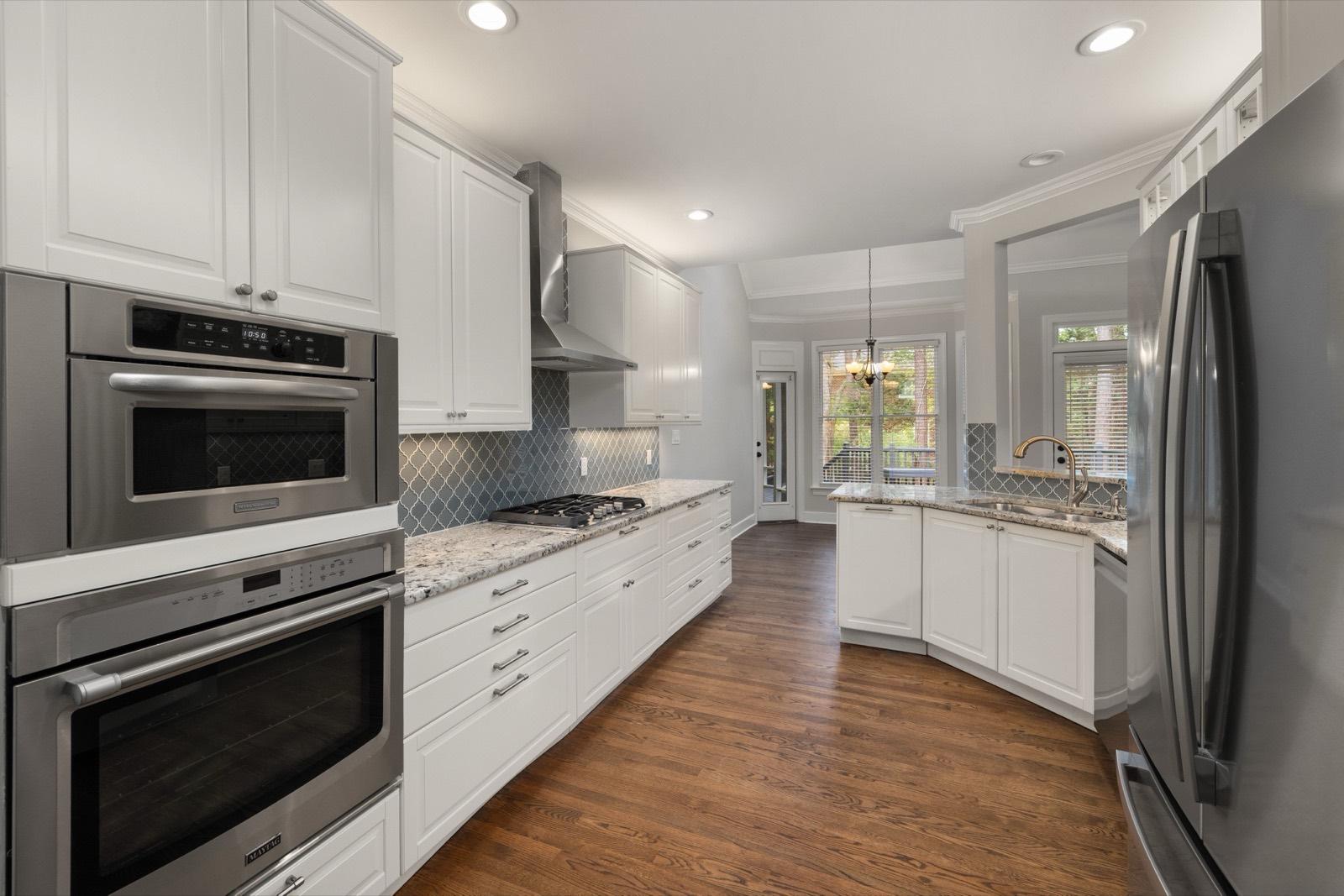 White galley kitchen with stacked wall ovens and hardwood floors — AMV Construction, Charlotte NC